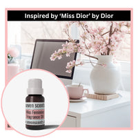 Desk setup with a vase of flowers, computer, and Seven Scents miss feminine fragrance oil inspireed by 'Miss Dior' by Dior.